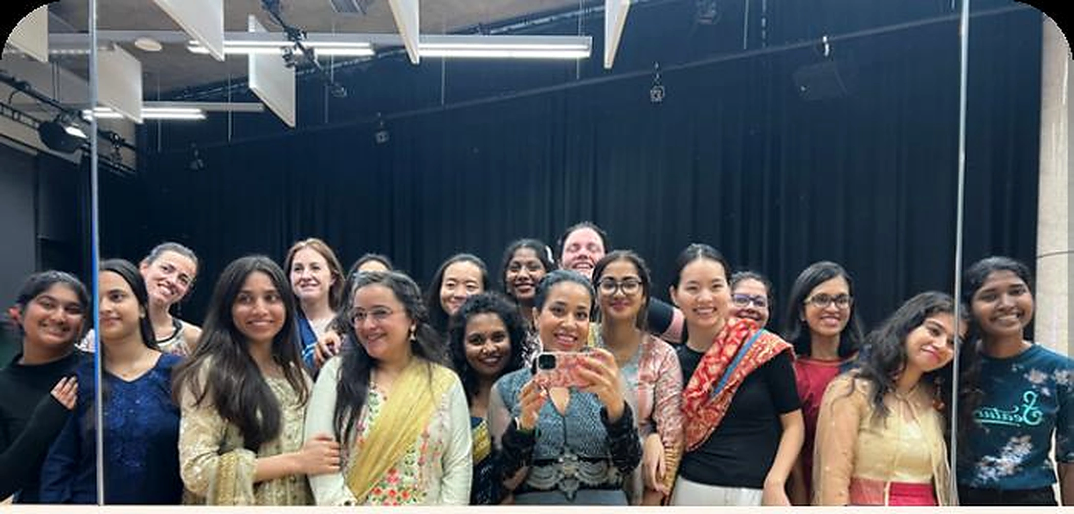 A diverse group of BollyFusion workshop participants smiling together in a dance studio